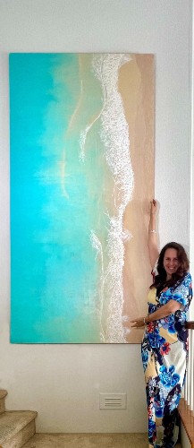 Lorena standing beside one of her large ocean paintings